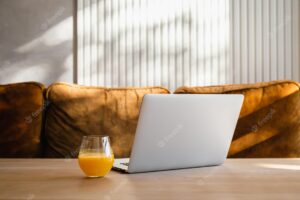 A glass of orange juice near the laptop on the table