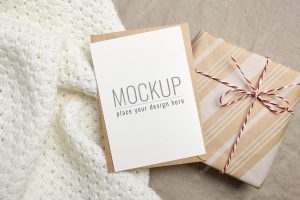 Greeting card mockup with gift box on knitted and linen background