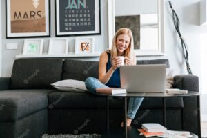 Happy woman with cup of coffee sitting and using laptop