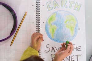 Horizontal banner or header with top view of child girl draws planet earth with wax colors on school notebook for earth day little activist girl writes the message save the planet