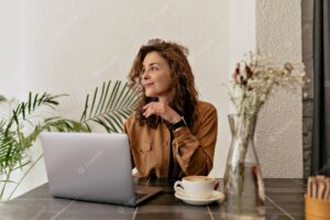 Joyful young woman looking aside sitting on table with laptop and smiling brunette with curly hair wears casual clothes positive emotions concept