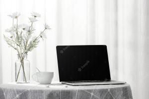 Laptop and a cup of coffee next to a vase full of flowers, indoors
