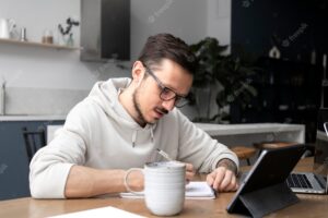 Man working from home at desk on tablet and writing