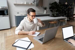Man working from home at desk while having a drink