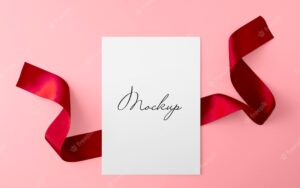 Paper sheet with red ribbon over pink surface mockup