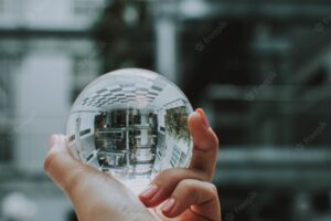 A person holding a clear crystal glass ball with the reflection of a building