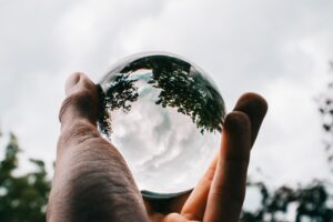 A person holding a glass ball with the reflection of beautiful green trees and breathtaking clouds