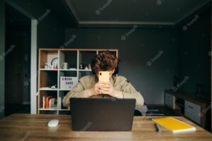 Remote worker at home sits at a desk with a laptop holds a smartphone and hides