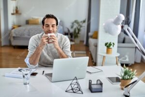 Smiling businessman enjoying in coffee break with his eyes closed while working at home