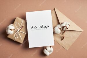 Stationary invitation or greeting card mockup with envelope, gift box and natural cotton plant flowers