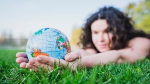 Woman lying on green grass holding globe in hand over green grass