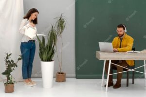 Woman watering plant and man using laptop