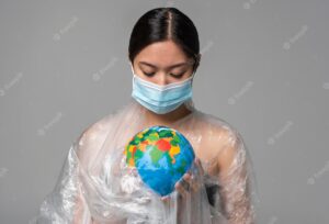 Woman with medical mask holding an earth globe while being covered in plastic