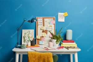Work place of student. desktop with lamp, opened notebook, stationery and green indoor plant, mug of coffee sticky notes on blue. home office