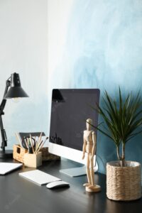 Workplace with computer, wooden man and plant on black wood table, copy space