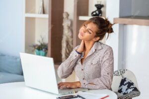 Young businesswoman suffering from neckache massaging her neck while sitting at her working place in home office
