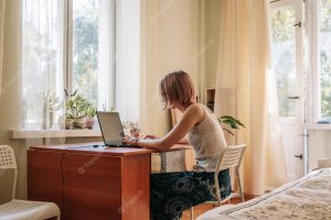 Young woman sitting by window working studying or surfing with laptop