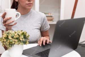 Front view of woman working on laptop while holding mug
