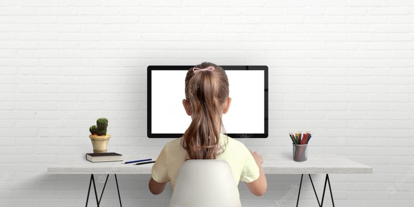 Girl is studying and working on the computer the concept of using modern technologies for children work desk in the room with books and pens