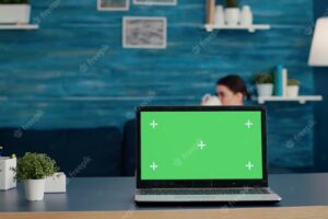 Laptop display with green screen background on desk, used to create mockup template and blank copy space with isolated chroma key. modern technology on computer in living room.