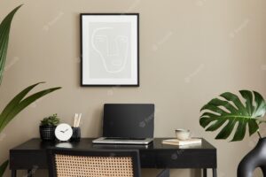 Stylish composition of home office interior with black wooden desk, chair, tropical flower in vase, laptop, frame, cup of coffee, clock and elegant office accessories..