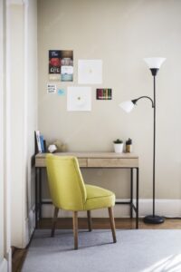 Vertical shot of a yellow chair and tall lamp near a wooden table with books and plant pots on it